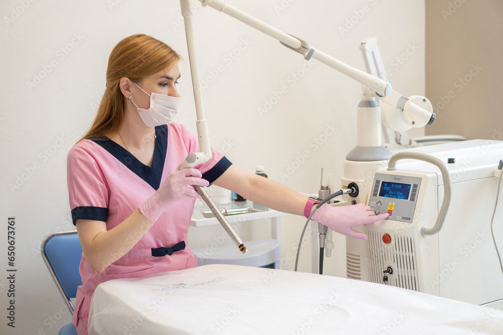 A middle-aged red-haired woman doctor of laser gynecology presses buttons on the screen of the Fotona laser device. Concept of laser technology in gynecology and women's health. A middle-aged red-haired woman doctor of laser gynecology presses buttons on the screen of the Fotona laser device. Concept of laser technology in gynecology and women's health.