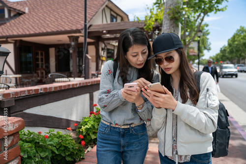 asian japanese woman visitor teaching her travel mate how to use navigation app on smartphone while they are touring downtown solvangin California usa photo