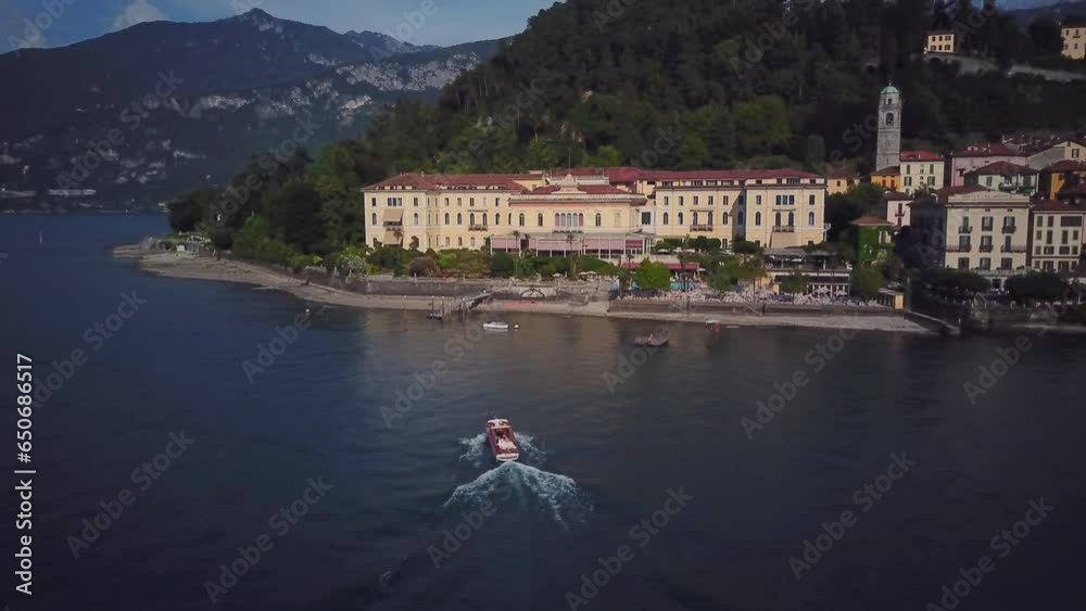 Drone Shot of Small Boat Sails Up to Villa. Yacht on Lake Como Moored to House. Aerial View of Yacht with a White Sail on Lake Como. Vacation in italy Concept