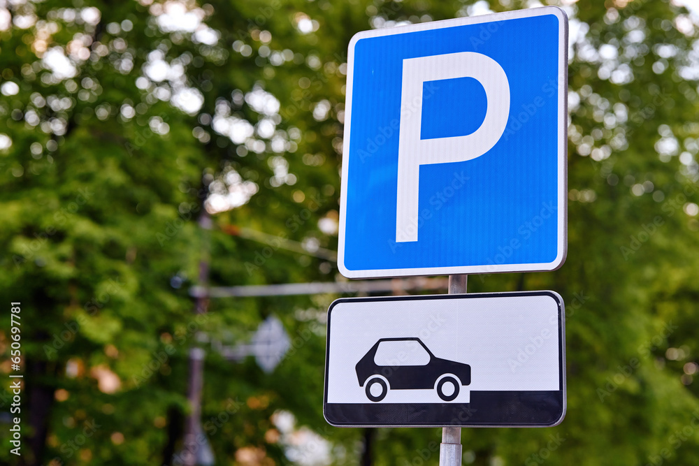 Road sign - Parking sign in the city. Parking zone for cars. Parking sign on the background of trees. Road sign - Parking sign in the city. Parking zone for cars. Parking sign on the background of trees.