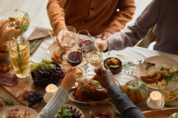 Diverse group of people toasting with wine glasses at festive dinner table celebrating Thanksgiving together, copy space