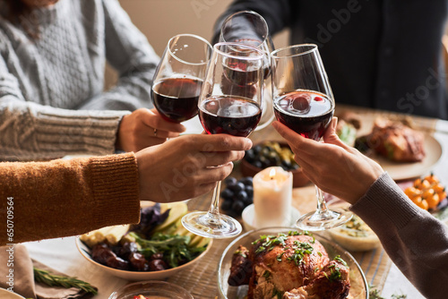 Side view closeup of friends clinking red wine glasses while celebrating at festive dinner table, copy space