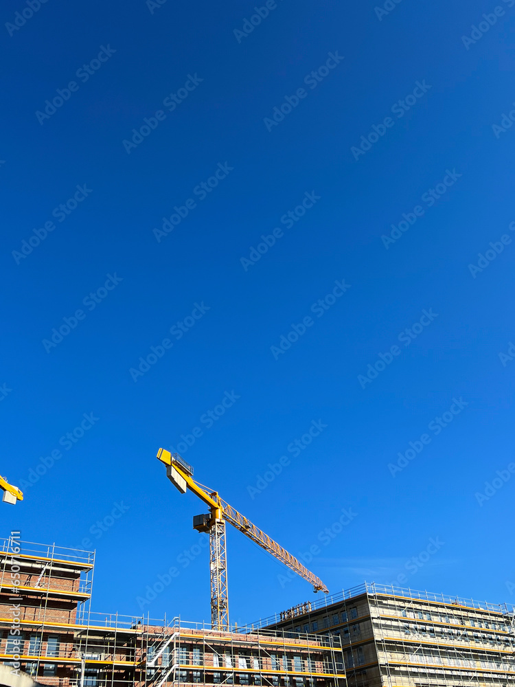 Fototapeta premium Construction site of a building in good weather. Yellow construction cranes on a working day. Construction of multi-storey buildings.