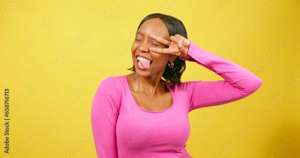 Happy young woman holds peace sign to eye, silly pose, yellow studio portrait Happy young woman holds peace sign to eye, silly pose, yellow studio portrait