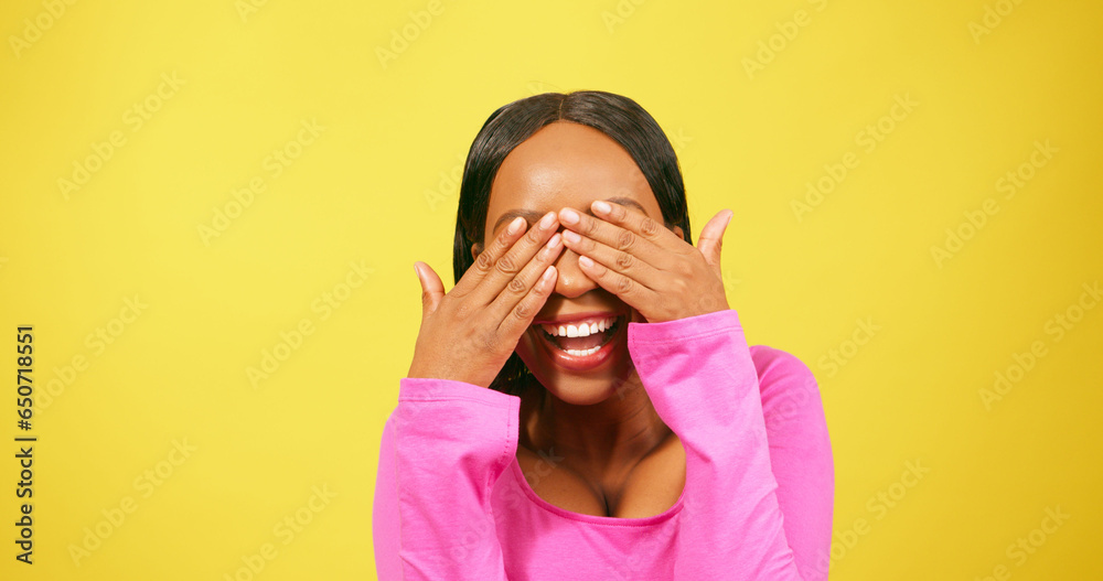 Beautiful young woman covers eyes, laughing, smiling, yellow studio background