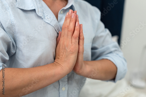 Closeup of peaceful millennial woman meditating, mental health. Woman holding hands in namaste gesture meditate, mental balance, time for herself. Stress relief, mediation, mind fullness concept.