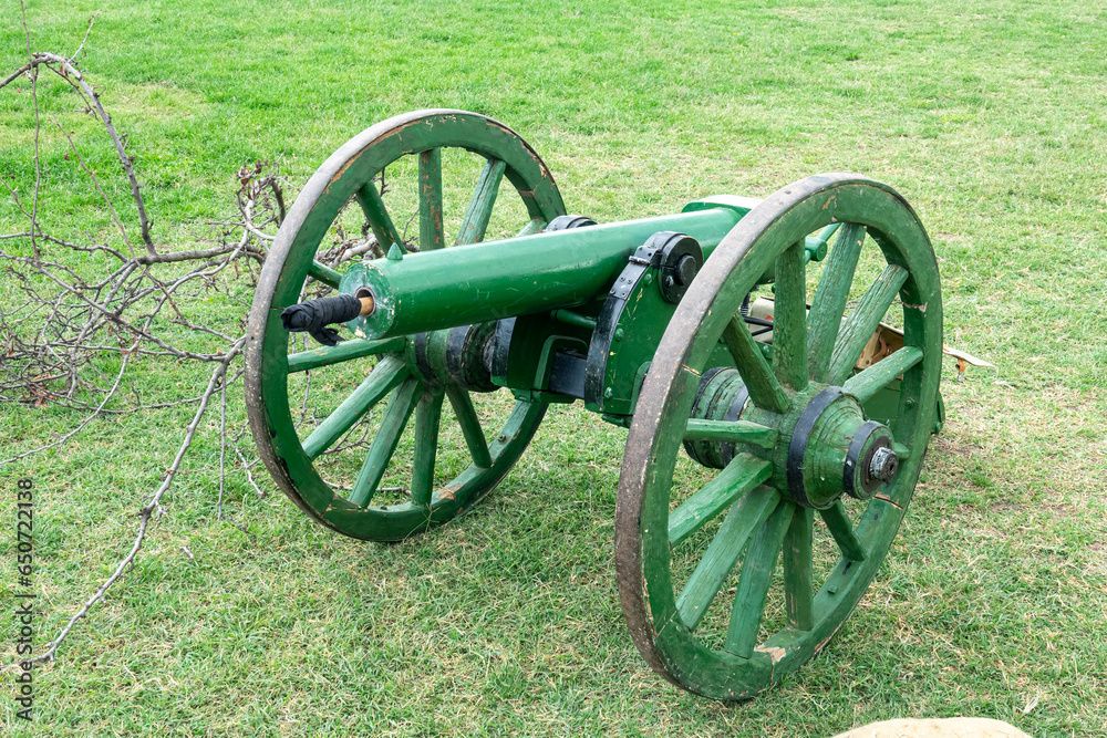 Old antique cannon with wooden wheels on grass.