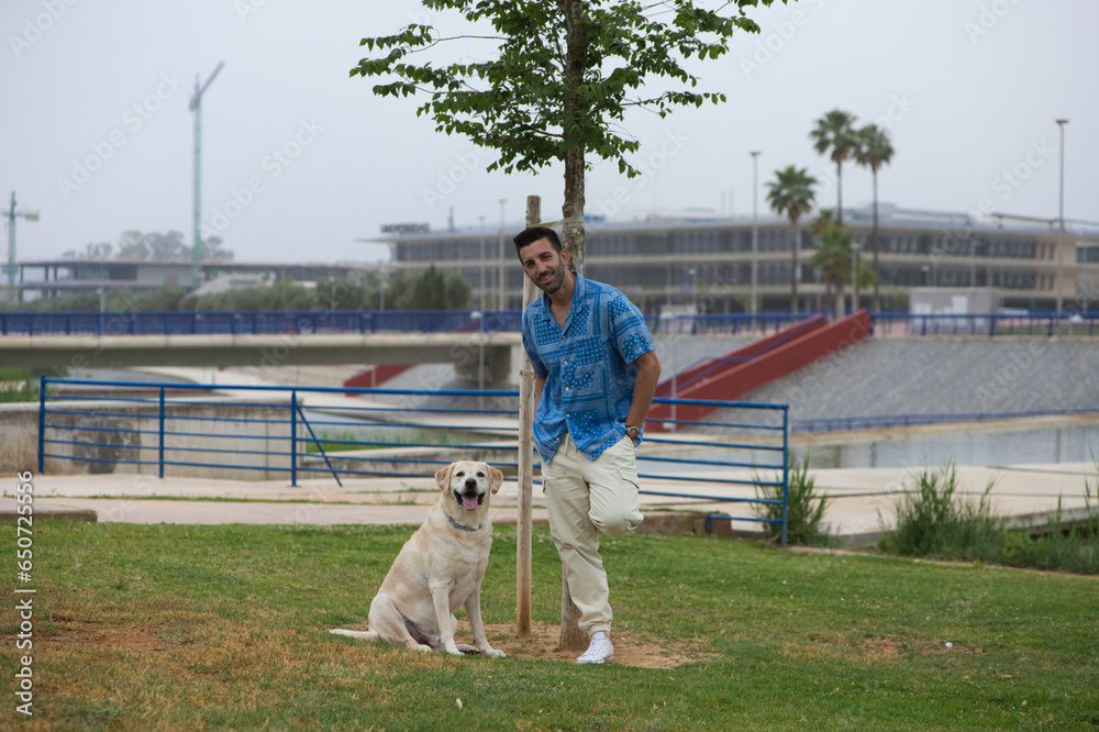 Handsome young man with beard walks with his large dog. The dog is a brown Labrador Retrievier. Concept pets and companion animals. International dog day. Handsome young man with beard walks with his large dog. The dog is a brown Labrador Retrievier. Concept pets and companion animals. International dog day.