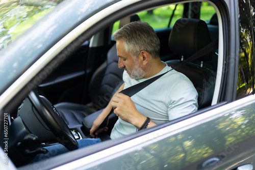 Caucasian man of middle age fasten seat belts in car before drive
