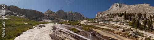 Panorama shot of colorful granite rocks and water over them. Blue sky and tops of Mount Whitney, usa