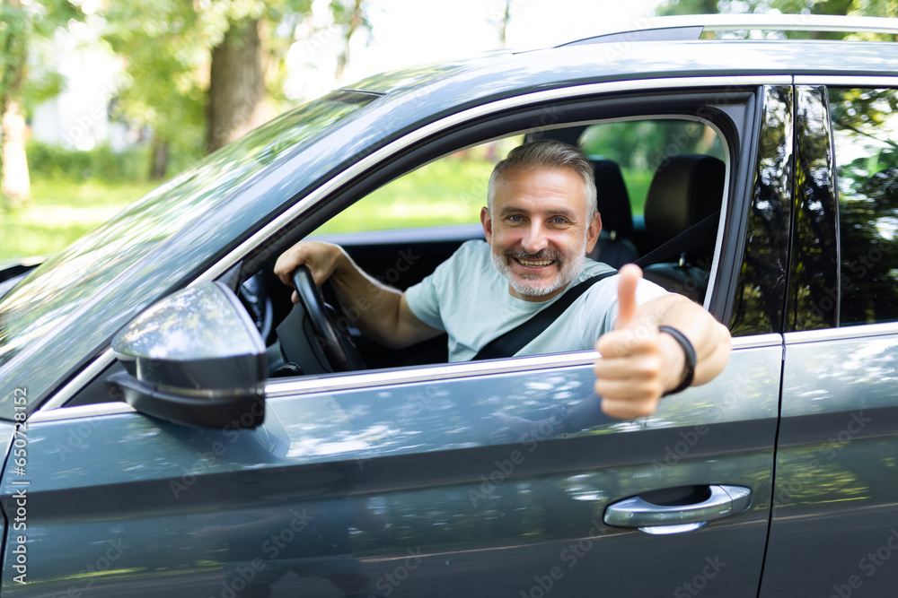 Middle age man make selfie by camera doing ok gesture while drive car at street
