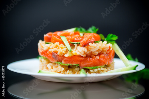 Boiled white rice with salted red fish, cucumbers and other vegetables with herbs in a plate.
