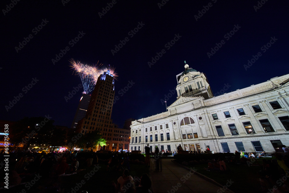 Naklejka premium Fireworks at night behind Lincoln Tower with people crowding courthouse lawn downtown Fort Wayne