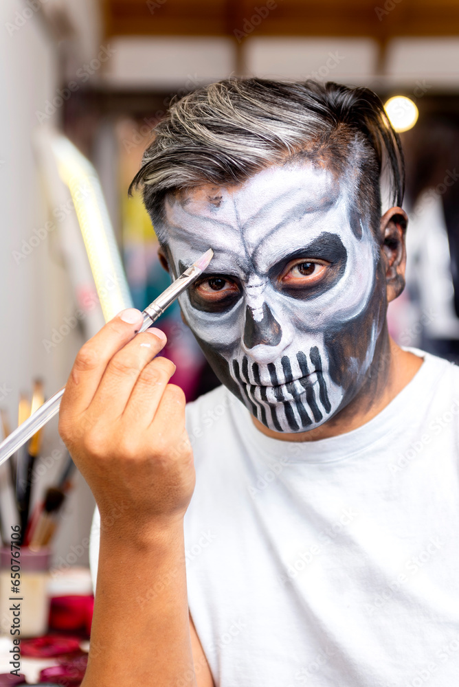 Latin man putting on makeup to celebrate Halloween or Days of the Dead Latin man putting on makeup to celebrate Halloween or Days of the Dead