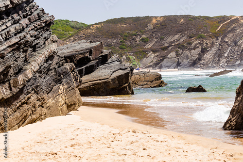 View of empty Praia da Amalia beach with ocean waves, cliffs and stones, wet golden sand and green vegetation at wild Rota Vicentina coast, Odemira, Portugal photo