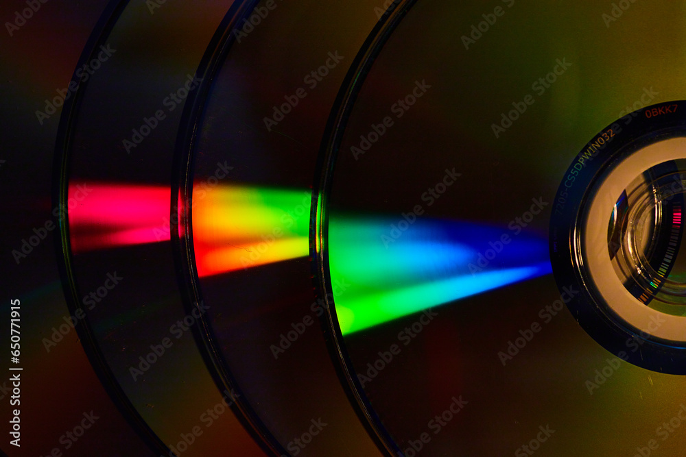 Abstract stack of four dark silvery CDs with reflective rainbow bursts of light on surface Abstract stack of four dark silvery CDs with reflective rainbow bursts of light on surface