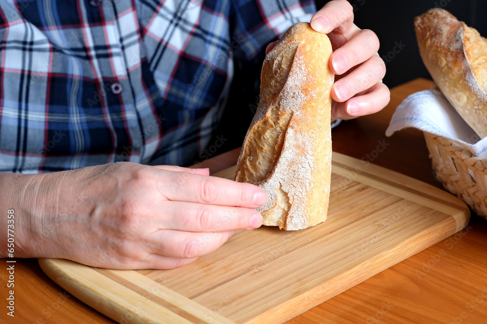 Hands of an elderly woman holding sliced white wheat bread baguette