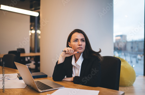Thoughtful woman sitting with laptop in office