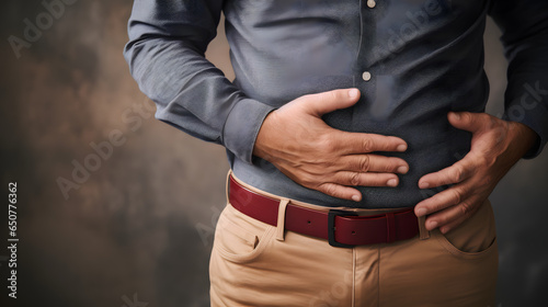 Close-up of a man holding his hands on his painfully hurting stomach experiencing abdominal pain and discomfort