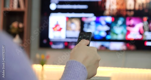 Close up hands of women choosing movie on internet streaming service. Women using remote control to select online movie streaming platform from television. Demand service on smart TV