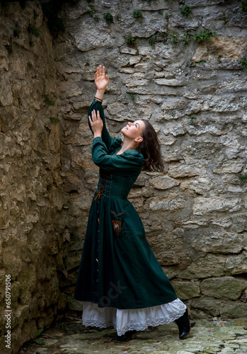 beautiful brunette woman in long green vintage dress posing in ancient castle 