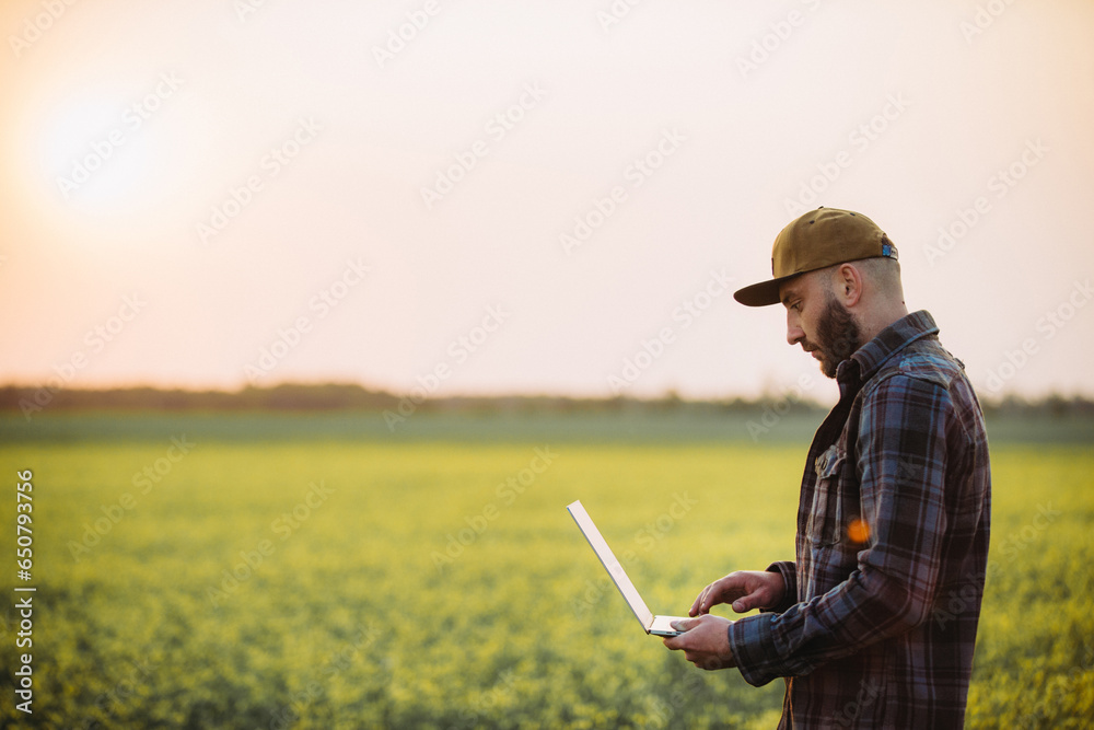 Farmer holding laptop,tablet in rapeseed field, to use a fertilization log program. Plant growth, production and contact online customer.