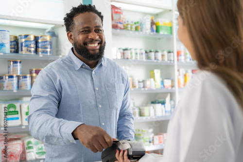 A man buys medicine in a pharmacy. He using credit card to pay drug with smiling in pharmacy.