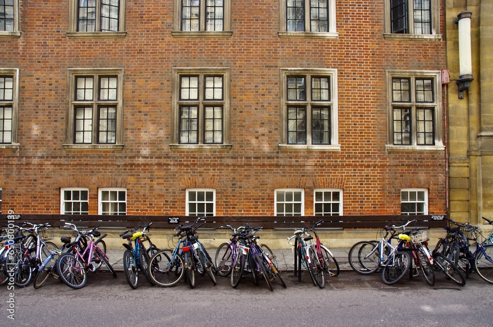A row of Bicycles with red brick building behind. 
