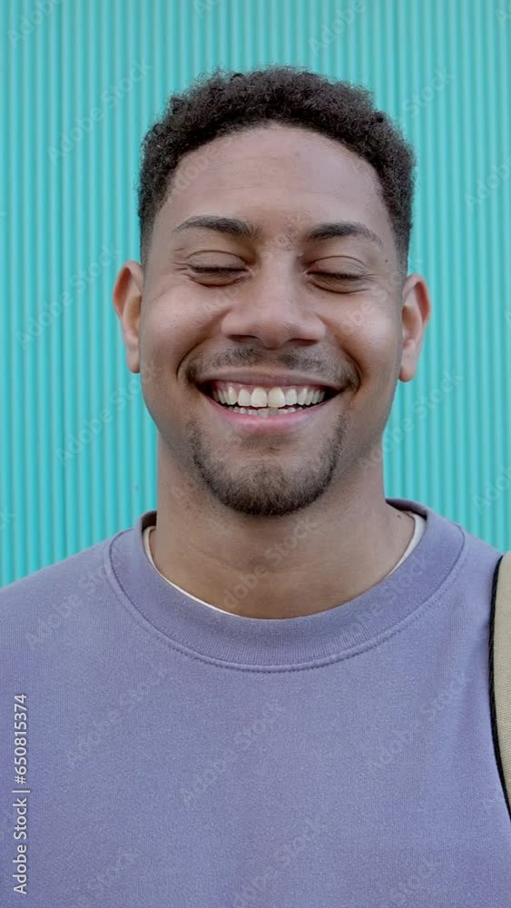 Happy young latin student smiling at camera standing over aquamarine building college wall background. Vertical screen 9:16 aspect video footage. Happy young latin student smiling at camera standing over aquamarine building college wall background. Vertical screen 9:16 aspect video footage.