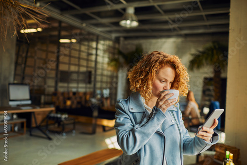 Young Caucasian woman drinking coffee and using a smartphone in a startup company office
