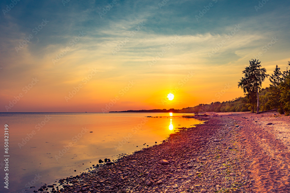 Sunset over the sea. Cloudy sky. Rocky shore. Smooth surface of water. Russia, Europe.