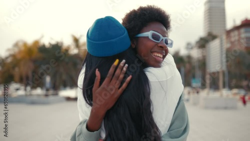 African American and Asian young cute women girlfriends hugging and having fun outdoors listening to music in headphones.