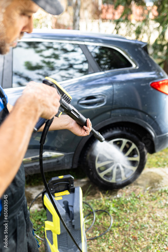 Worker washing or spraying car wheel with high pressure washer outdoors.