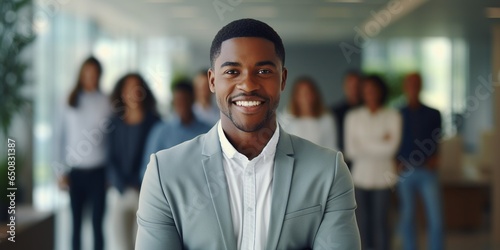 Confident young African American businessman standing in front of his team on blurred modern office background with copy space.