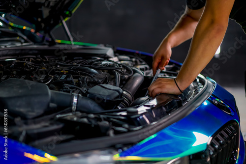 A car service worker with a wrench in his hands fixes a car in chamillion-colored film with the hood open 