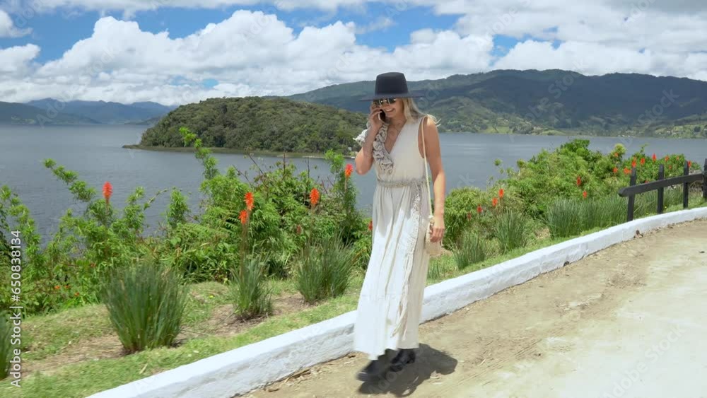 LATIN WOMAN TALKING ON CELL PHONE IN BEAUTIFUL LANDSCAPE OF LA LAGOON DE LA COCHA PASTO NARIÑO. WALK IN LAKE GUAMUEZ WITH HANDMADE BAG