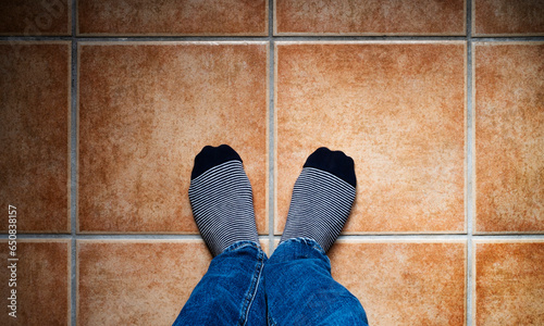 Image from above of two feet with striped socks on a tiled floor in warm tones. Selfie concept.