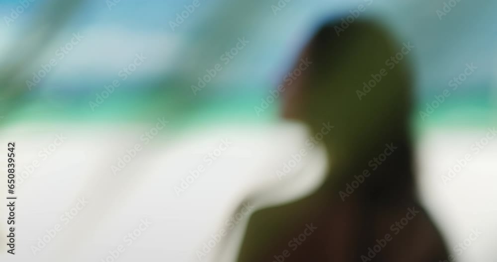 Woman close up relax behind palm tree leaf swaying in the wind with sun light. Portrait of brunette girl back view on Boracay tropical island beach. Summer vacation concept. Zoom in slow motion