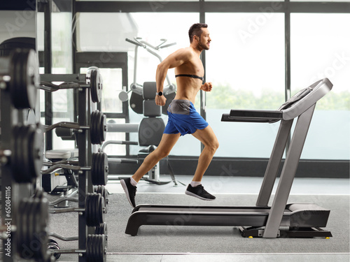 Young man running on a treadmill and wearing a chest strap at the gym