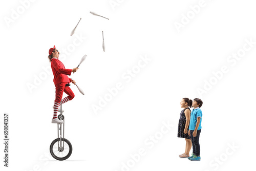 Children watching an acrobat riding a giraffe unicycle and juggling