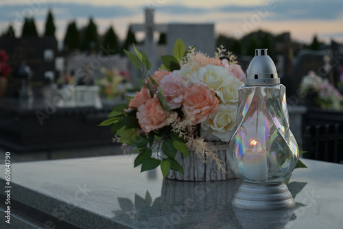 Candle and flowers on the tomb with cemetery in the background.