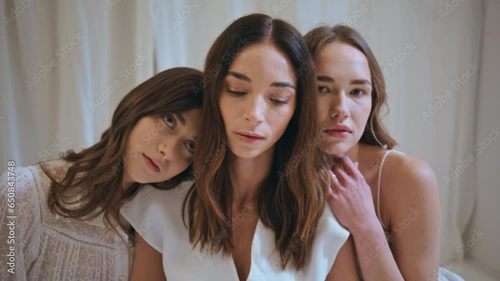 Portrait three women embracing in cozy room. Serene beautiful girls look camera Portrait three women embracing in cozy room. Serene beautiful girls look camera