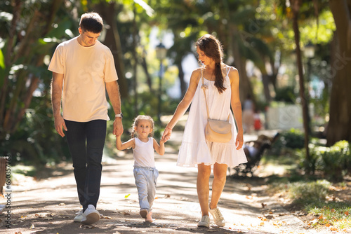 Young family walking in a summer park holding hands