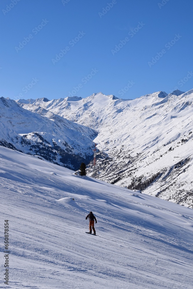 Skiers and snowboarders in Hochgurgl ski resort, backdropped by the Ötztal valley and the snow capped alpine mountains in Tyrol, Austria on a beautiful sunny day, perfect conditions for winter sports.