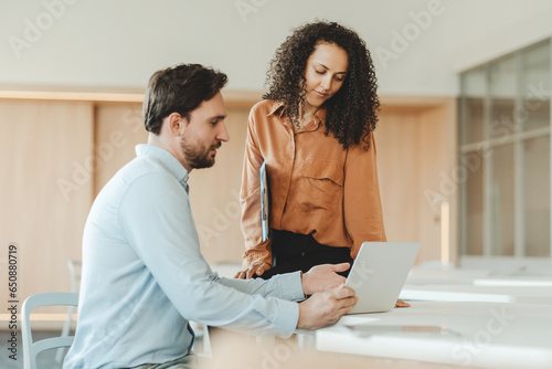 Positive African American woman and hispanic man using laptop, sitting at workplace in modern office
