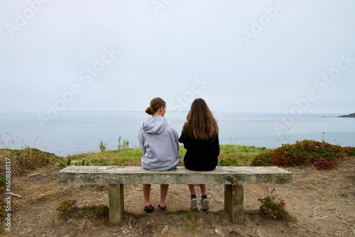 Rear view of two young female friends sitting on a beachside bench