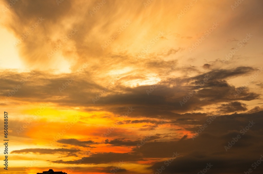 Fototapeta premium Vibrant orange sky at sunset illuminated with white and grey clouds