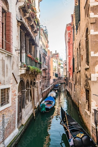 Row of small boats is moored along a picturesque canal in a bustling cityscape in Venice, Italy