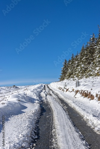 Beautiful scene showcases a scenic winter road winding around a rolling hill © Jakub Szoska/Wirestock Creators