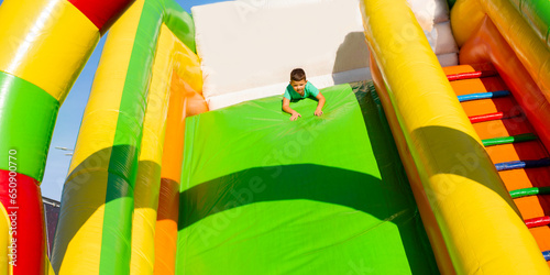 Little boy child ride upside down on an inflatable multi-colored slide. Sliding head down 